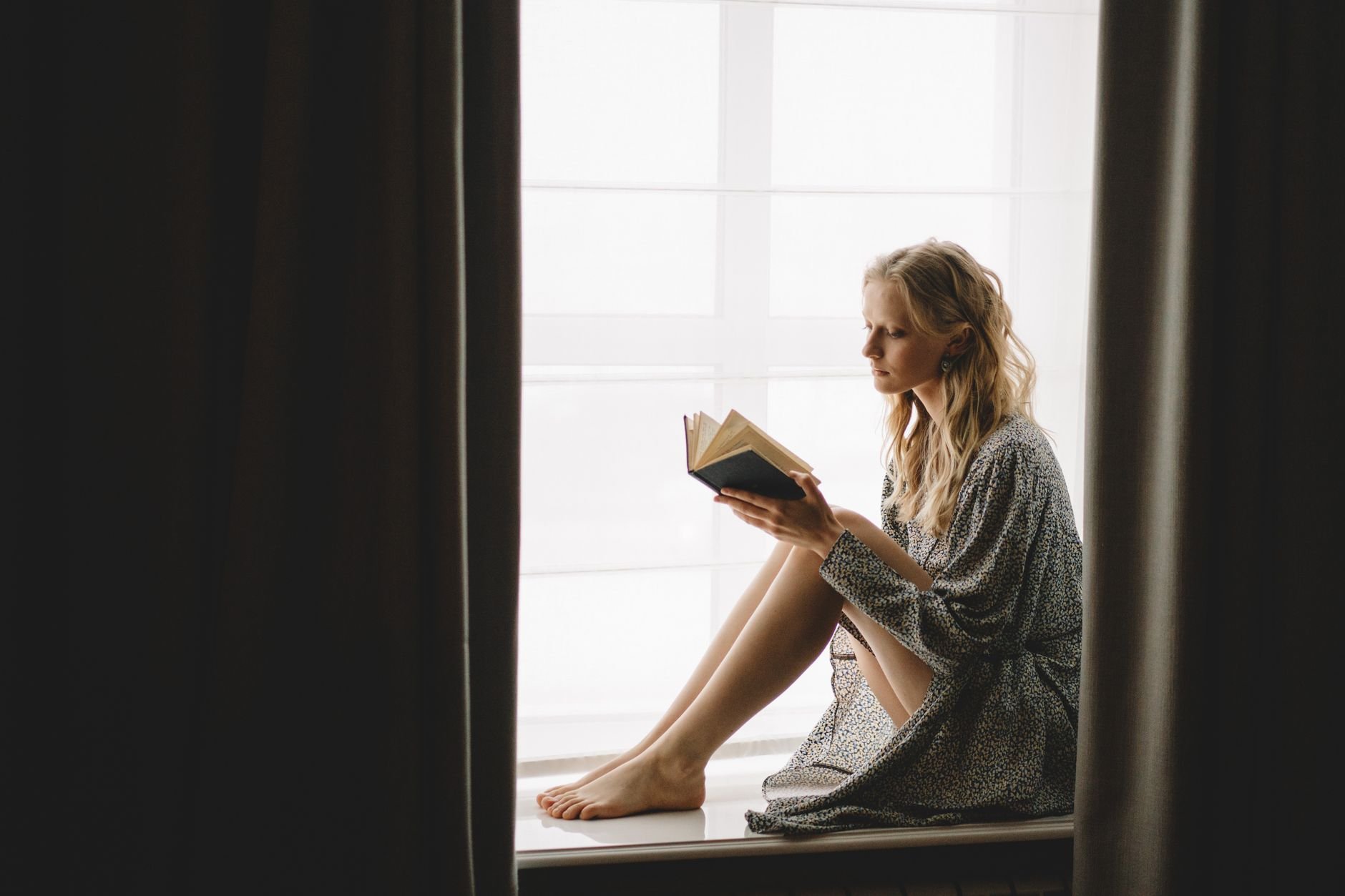 A young woman reading peacefully by a window in soft morning light